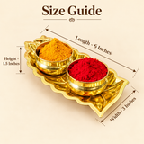 Size guide image of a brass Haldi Kumkum bowl set showing a leaf-shaped brass tray measuring 6 inches in length, 4 inches in width and approximately 2 inches in overall height. The polished brass tray holds two round bowls containing yellow haldi and red kumkum powders, displayed against a neutral beige background with clear measurement arrows.