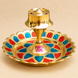 Traditional Brass Incense Stick Holder featuring a polished golden brass finish, circular decorative tray with vibrant red and blue Meenakari-style detailing, scalloped edges and a raised central agarbatti holder with multiple incense stick holes. Measuring 3.5 inches in diameter and 2 inches in height, this decorative brass agarbatti stand is suitable for daily pooja, home mandir decoration, incense burning, religious ceremonies, festive arrangements and traditional Indian home decor.