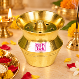Traditional Brass Kalash Shape pooja holder displayed in an elegant home worship setting with warm lighting, fresh marigold flowers, brass pooja accessories, and decorative religious offerings. The golden brass item features a wide flared opening, central raised holder, circular holes, and distinctive kalash-shaped body, creating a beautiful addition to home mandir arrangements, everyday prayers, festive decorations, and traditional religious ceremonies.
