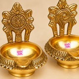 Close-up image of Brass Kuber Diya set of 2 showing the intricate embossed floral backplate, curved spout, deep oil bowl and textured decorative rim. The polished brass finish and detailed traditional craftsmanship are clearly visible, making the diyas suitable for pooja and festive home decor.