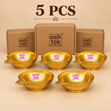 Brass Kuber Diya Pack of 5 Pcs featuring five matching traditional golden brass pooja oil lamps arranged neatly in two rows, with three diyas positioned at the back and two in front, alongside simple brown cardboard packaging boxes against a premium beige studio background. Each brass Kuber diya features a smooth rounded oil-holding bowl, polished reflective golden interior, distinctive pointed wick spout, decorative engraved geometric patterns around the outer surface, and a compact circular base.
