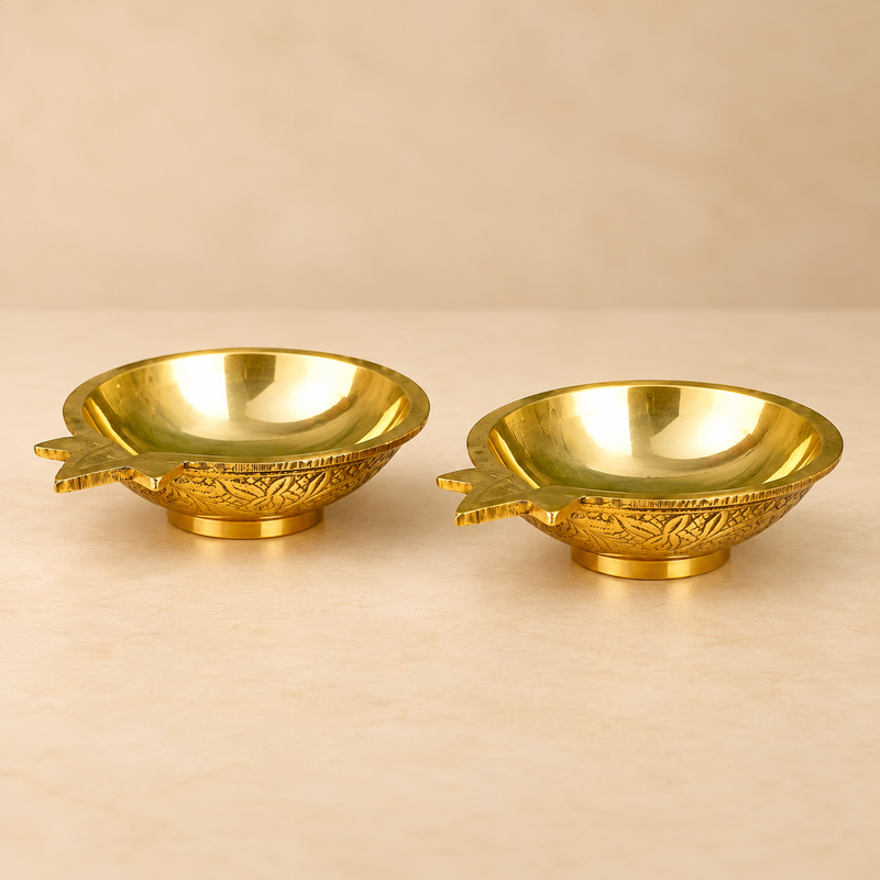 Brass Kuber Diya Set of 2 Pcs featuring two matching traditional brass pooja oil lamps with a polished golden brass finish, smooth shallow bowl-shaped oil reservoirs, decorative pointed star-shaped wick spouts, intricately engraved floral patterns around the outer surfaces, and sturdy circular pedestal bases. Each brass diya measures 3 inches in length, 2.5 inches in width, and 1 inch in height. Displayed together against a premium beige studio background, these traditional brass Kuber diyas are suitable fo