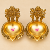 Top and angled view of Brass Kuber Diya set of 2 showing the round brass bowl, pointed front spout, decorative outer border and upright floral backplate. These traditional brass diyas are compact in size and suitable for pooja setups, festival decoration and home temple display.