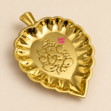 Brass leaf tray with a polished golden finish, decorative leaf-shaped form, scalloped raised rim and embossed Ganesh design in the center, professionally presented on a premium beige studio background for puja, festive decor and gifting.