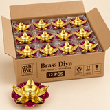 Twelve piece bulk gifting pack of decorative brass lotus diyas arranged neatly inside an open cardboard box, showing the golden brass oil bowls, central wick holders, gold leaf shaped lotus petals and vibrant magenta floral bases with protective packaging, designed for convenient bulk ordering for Diwali, puja ceremonies, festive return gifts, weddings, housewarming events and corporate gifting.