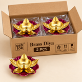 Open cardboard bulk packaging box containing 2 decorative brass lotus diyas individually protected for transport, each diya featuring a polished golden brass bowl, central wick holder, gold lotus leaf petals and magenta flower shaped base, with one product displayed outside the box to show the actual design, suitable for festive gifting, puja events, return gifts and bulk Diwali purchases.