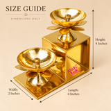 Brass Lotus Diya with Stand size guide showing a two-step golden brass oil lamp arrangement with clearly marked measurements of 4 inches length, 2 inches width and 4 inches height. The decorative stepped structure holds two traditional lotus-shaped diya bowls at different elevations, each featuring a central wick holder, smooth polished interior, petal-shaped decorative support and sturdy pedestal. The dimensional illustration highlights the compact rectangular frame and elegant tiered arrangement, suitable
