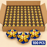 Bulk pack of 100 traditional brass lotus diyas featuring polished golden brass oil bowls with central wick holders, elegantly curved golden lotus petals and royal blue decorative flower-shaped bases. The image shows a large open brown corrugated cardboard box with multiple compartmentalized rows of diyas and three display pieces in front. Suitable for bulk Diwali gifting, wedding return gifts, religious ceremonies, festive events and large-scale decorative puja arrangements.