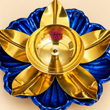 Detailed close-up view of a traditional brass lotus diya showcasing its polished golden brass oil bowl, circular inner detailing, raised central wick holder and elegantly shaped golden lotus petals. The diya features a deep royal blue decorative floral base with textured petals and scalloped edges, highlighting the contrasting metallic finishes and intricate flower-shaped design suitable for puja and Diwali decoration.