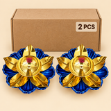 Set of 2 traditional brass lotus diyas featuring polished golden brass bowls with central wick holders, curved golden lotus petals and vibrant royal blue flower-shaped decorative bases. Both diyas are displayed in front of a simple brown cardboard packaging box. Each diya measures 6 inches in diameter and 1.5 inches in height, suitable for daily puja, Diwali decorations, festive gifting and home mandir arrangements