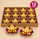 Set of 12 traditional brass lotus diyas featuring golden lotus petals, a central oil-holding bowl with a wick holder and a decorative pink floral base. Arranged in a simple cardboard box with individual compartments for protection, suitable for Diwali decorations, daily puja, festive gifting and religious ceremonies