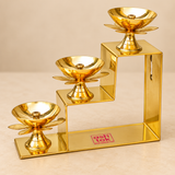 Brass Lotus Diya with Stand in a decorative 3 Step variant featuring three golden brass lotus-shaped oil lamps arranged across three ascending levels of a polished geometric staircase structure. Each diya features a round reflective oil bowl, central wick holder, lotus flower petal support and elegant pedestal base. The three lamps are positioned at progressively increasing heights, creating a symmetrical decorative display with a traditional brass finish. Suitable for home decoration, festive lighting.