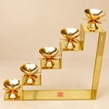 Brass Lotus Diya with Stand featuring a five-step golden brass staircase arrangement holding five individual lotus-shaped oil lamps at progressively increasing heights. Each brass diya includes a smooth polished circular oil bowl, central wick holder, decorative lotus petals beneath the bowl and a shaped pedestal support. The geometric five-level stand features a long rectangular base with a reflective golden brass surface, creating an elegant decorative display suitable for festive lighting, Diwali celebra