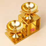 Top angled view of the Brass Lotus Diya with Stand featuring two polished golden brass oil lamps mounted on a decorative two-step geometric frame. The elevated perspective clearly shows the wide circular diya bowls, central wick holders, smooth reflective brass interiors and lotus-shaped petals beneath each holder. The arrangement features one diya at the lower level and another at the upper level, supported by a rectangular metal structure with a bright golden finish. Ideal for displaying the detailed cons