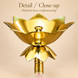 Close-up image of the Brass Lotus Stand Diya showing the polished brass craftsmanship, curved lotus petals, central wick holder, smooth reflective bowl, decorative lower lotus section and turned stem detailing, captured against a beige background to emphasize the product’s finish, shape, construction and traditional ornamental styling.