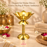 Brass Lotus Stand Diya displayed with a lit flame in a warm home décor setting, surrounded by flowers, decorative brass accents and soft ambient lighting, showing how the polished lotus-shaped diya can be used for festive styling, elegant table décor, warm home ambience and special occasions.