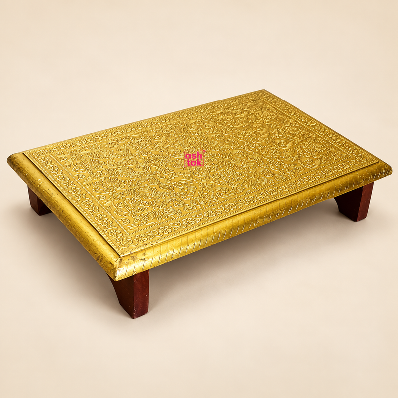 Traditional Brass Marriage Chowki featuring a beautifully embossed golden brass sheet surface with intricate floral patterns, decorative vine motifs and detailed ornamental borders. The rectangular platform is supported by four short dark brown wooden legs that provide an elevated traditional seating or ceremonial surface. The handcrafted golden top features finely engraved decorative edges and a raised floral pattern across the entire surface.
