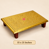 12 × 18 inch traditional Brass Marriage Pita Chowki presented against a soft beige studio background with a clearly visible size label. The rectangular platform features an intricately embossed golden brass sheet surface decorated with traditional floral patterns, scrolling vine motifs and finely detailed ornamental borders. The raised platform rests on four dark brown wooden legs and features polished golden edges with decorative engraved detailing. Suitable for Indian marriage ceremonies.