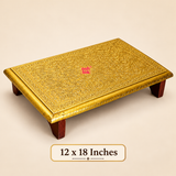 15 × 21 inch traditional Brass Marriage Chowki featuring a rectangular golden brass sheet-covered platform with elaborate embossed floral designs, decorative vine patterns, ornamental borders and polished golden edges. The platform is supported by four sturdy dark brown wooden legs, creating a low traditional ceremonial stand. Photographed against a warm beige studio background with a clearly displayed size label, highlighting its decorative surface and rectangular proportions.