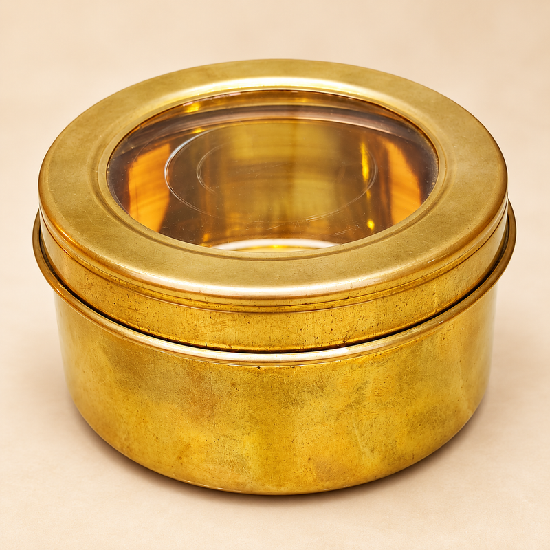 Traditional round brass masala box featuring a golden brass finish, smooth cylindrical body and removable circular lid with a transparent viewing window. The 6-inch diameter and 3-inch height brass storage container has a broad metallic lid rim and a compact design suitable for organizing Indian kitchen spices, dry fruits, small household essentials and traditional kitchen accessories.