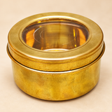 Traditional round brass masala box featuring a golden brass finish, smooth cylindrical body and removable circular lid with a transparent viewing window. The 6-inch diameter and 3-inch height brass storage container has a broad metallic lid rim and a compact design suitable for organizing Indian kitchen spices, dry fruits, small household essentials and traditional kitchen accessories.