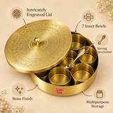 Features infographic of a traditional brass masala box highlighting its intricately engraved decorative lid, seven removable inner bowls, included serving spoon, polished brass finish and multipurpose spice storage design. The round spice box is shown open on a premium beige background so the individual containers and inner arrangement can be clearly viewed.