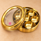 Detailed close-up of brass masala box highlighting the transparent glass lid, polished brass rim, seven removable inner bowls, smooth golden finish and traditional round spice box construction.