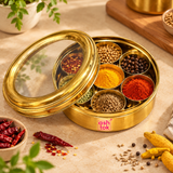 Brass masala box shown with seven compartments filled with turmeric, chilli powder, cumin, coriander, pepper and other spices in a premium kitchen setting for everyday spice storage and cooking use.