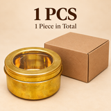 Single traditional brass masala storage box featuring a golden cylindrical body and a removable brass-framed transparent viewing lid, displayed beside a plain brown cardboard packaging box on a beige studio background. The container measures 6 inches in diameter and 3 inches in height, suitable for individual purchase, spice storage, dry fruit organization and everyday kitchen use.