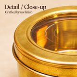 Detailed close-up view of a traditional brass masala storage box highlighting its golden brass surface texture, smooth rounded lid rim, transparent circular viewing window and precise lid-to-container fitting. The image showcases the metallic finish, subtle surface detailing and practical removable lid construction of the round brass storage container designed for storing kitchen spices, dry fruits and small household essentials.