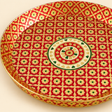 Detailed close-up photograph highlighting the intricate red and gold floral lattice work and central circular medallion pattern of a handcrafted brass Meenakari tray with raised sides, set on a cream background.