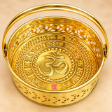 Detailed top view close-up of Brass Oval Shape Phool Butti, Temple Basket and Puja Butti showing the embossed Om symbol in the center, surrounding traditional decorative motifs, polished golden brass surface, oval inner shape, patterned cutwork walls and curved carrying handle. The close-up highlights the intricate craftsmanship, reflective brass finish and ASHTOK logo of this decorative puja and temple flower basket.