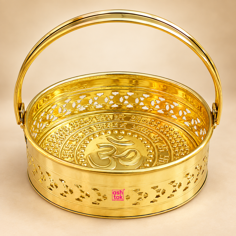 Brass Oval Shape Phool Butti, Temple Basket and Puja Butti featuring a polished golden brass finish, oval-shaped body, sturdy curved carrying handle, decorative cutwork pattern and embossed Om design inside the base. The ASHTOK logo is visible on the front, and the product is professionally displayed on a premium beige studio background for puja use, temple offerings, flower carrying, festive rituals and traditional home decor.