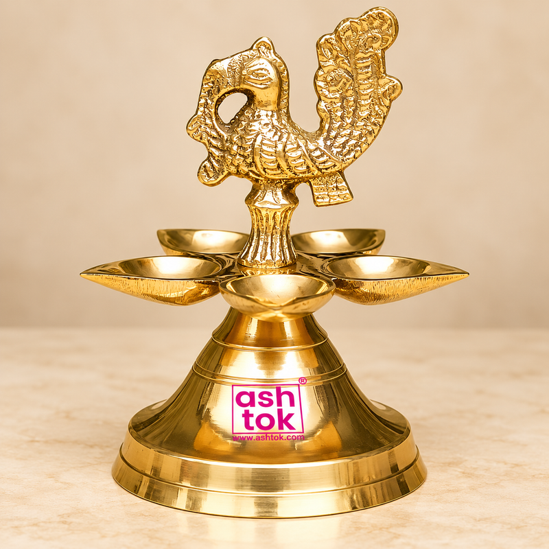 raditional Brass Panchmukhi Peacock Design Diya displayed in a premium beige studio setting, featuring an intricately detailed golden brass peacock figure rising above five beautifully arranged oil lamp bowls. The decorative peacock finial showcases carefully textured feathers, a gracefully curved neck, a distinctive head design, and an elaborate raised tail with ornamental patterns that enhance the traditional appearance of the lamp. Five shallow brass diya bowls surround the central column in a symmetrica
