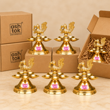 Multiple traditional Brass Panchmukhi Peacock Design Diyas displayed together in a professional bulk gifting presentation with simple brown cardboard packaging against a premium beige studio background. Each polished golden brass diya features a beautifully detailed peacock finial with ornamental feather carvings, a curved neck, a distinctive head, and an elaborately textured raised tail. Five shallow brass oil lamp bowls surround the central supporting column, forming an attractive flower-like Panchmukhi