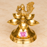 Elevated top-angled view of a traditional Brass Panchmukhi Peacock Design Diya highlighting the arrangement of five golden brass oil lamp bowls surrounding an intricately sculpted central peacock figure. The slightly elevated perspective clearly displays the five shallow diya bowls arranged in a flower-like circular pattern, each featuring a smooth concave interior, polished reflective surface, and gently pointed outer edge suitable for placing cotton wicks during traditional pooja rituals. 