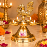 Traditional Brass Panchmukhi Peacock Design Diya beautifully illuminated with five glowing cotton wick flames in an elegant festive pooja setting, showcasing a polished golden brass oil lamp with an intricately sculpted peacock figure rising above five surrounding diya bowls. The decorative peacock features textured feather patterns, a curved neck, detailed wing carvings, and an elaborately raised tail, creating an attractive focal point above the illuminated oil lamps. Five shallow brass bowls arranged