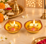 Two Brass Pankti Puja Diyas with glowing cotton wicks and flames arranged alongside flowers, brass pooja thali, kumkum and rice for traditional worship.