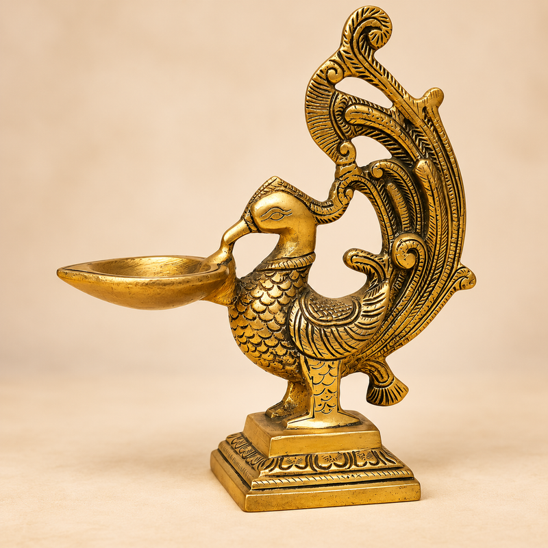 Angled product view of a traditional antique brass peacock diya with detailed carved peacock body and decorative tail.