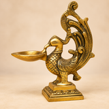 Angled product view of a traditional antique brass peacock diya with detailed carved peacock body and decorative tail.
