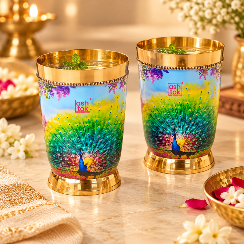 Peacock printed brass water glasses styled with chilled water, ice and fresh mint in an elegant festive setting, showing their use for serving water and beverages during celebrations, dining and special occasions.