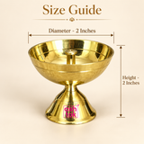 Product size guide diagram displaying a polished brass pedestal diya on a beige background with dimension arrows marking a diameter of 2 inches and a total height of 2 inches, complete with the Ashtok brand watermark.