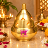 Traditional Brass Piyali Akhand Deep illuminated during a home temple pooja, featuring warm glowing light passing through the decorative star-shaped openings of its polished golden brass dome. Beautifully arranged alongside fresh marigold flowers, pooja offerings, and glowing traditional diyas, creating a devotional atmosphere for daily worship, Diwali celebrations, and religious ceremonies.