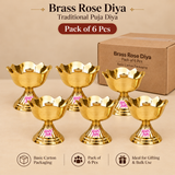 Brass Rose Diya pack of 6 pieces displayed on a premium beige studio background alongside simple brown cardboard carton packaging suitable for practical storage and bulk gifting. The image features six matching traditional brass pooja diyas arranged in two rows, each crafted with a polished golden finish, gracefully curved rose petal bowl, scalloped flower-shaped rim, decorative horizontal engraved lines, and a central cylindrical wick holder. Every diya rests on a sturdy fluted pedestal stand with a broad 