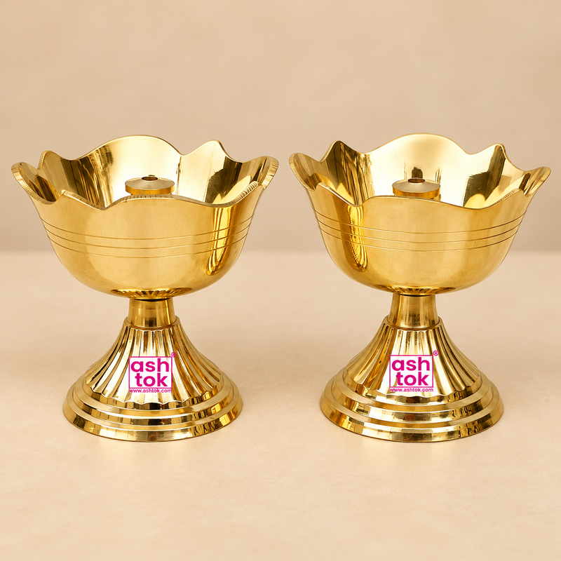 Two traditional Brass Rose Diyas displayed side by side on a premium beige studio background, featuring an elegant flower-shaped bowl with beautifully curved rose petal edges, a polished golden brass finish, and a central cylindrical wick holder designed for lighting during pooja rituals. Each brass diya features delicate horizontal engraved lines around the bowl, a sturdy fluted pedestal stand, and a broad circular stepped base with decorative concentric rings. The reflective golden surface highlights the 