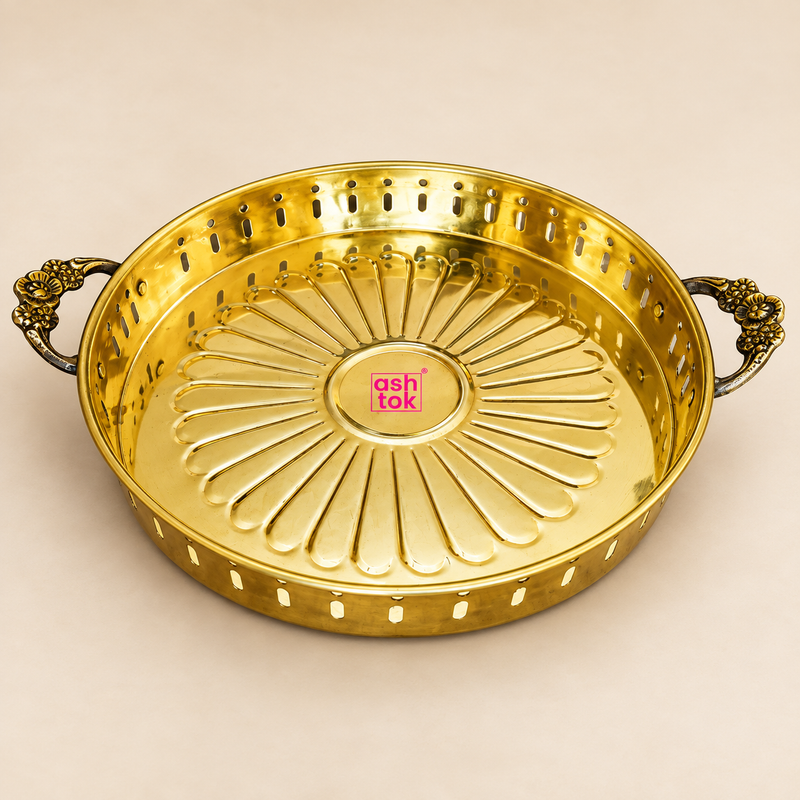 Premium round brass serving tray with two decorative floral side handles, polished golden finish, raised circular rim and elegant radial flower-petal embossed pattern across the base, photographed individually on a clean warm beige studio background. The tray has decorative perforated openings around the side wall and antique-style floral handles that provide a traditional handcrafted appearance.