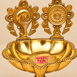 Close-up detail image of Brass Shanku Chakra Diya showing the intricate Shanku and Chakra motifs, polished brass finish, beaded rim, and scalloped diya bowl.