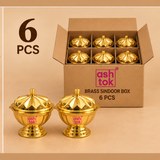 Six polished brass sindoor boxes packed neatly in a plain brown cardboard box with divider compartments, with two complete pieces displayed in front to highlight the rounded sindoor container body, decorative flower-inspired lid, small top knob, pedestal base and bright golden brass finish, shown on a soft beige background as a practical 6 piece quantity presentation suitable for pooja gifting, festive use, family functions, return gifts, retail packs and regular shipping without premium packaging.