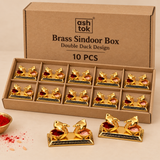 Ten-piece set of Brass Sindoor Box Double Duck Design arranged neatly inside a simple brown corrugated cardboard box with individual kraft divider compartments, with additional pieces displayed in front to clearly show the polished golden brass finish, paired duck-shaped containers, rectangular decorative base and open compartments filled with traditional red sindoor and light-colored ritual material, presented on a clean beige studio background for wholesale orders, festive distribution, wedding return gif