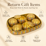 An promotional image for a return gift set featuring a decorative brass serving tray with six matching covered bowls arranged inside. The tray and bowls feature a multi-tone brass, copper, and silver textured band around the edges, with transparent glass lids on the bowls and a hammered interior texture on the golden tray.